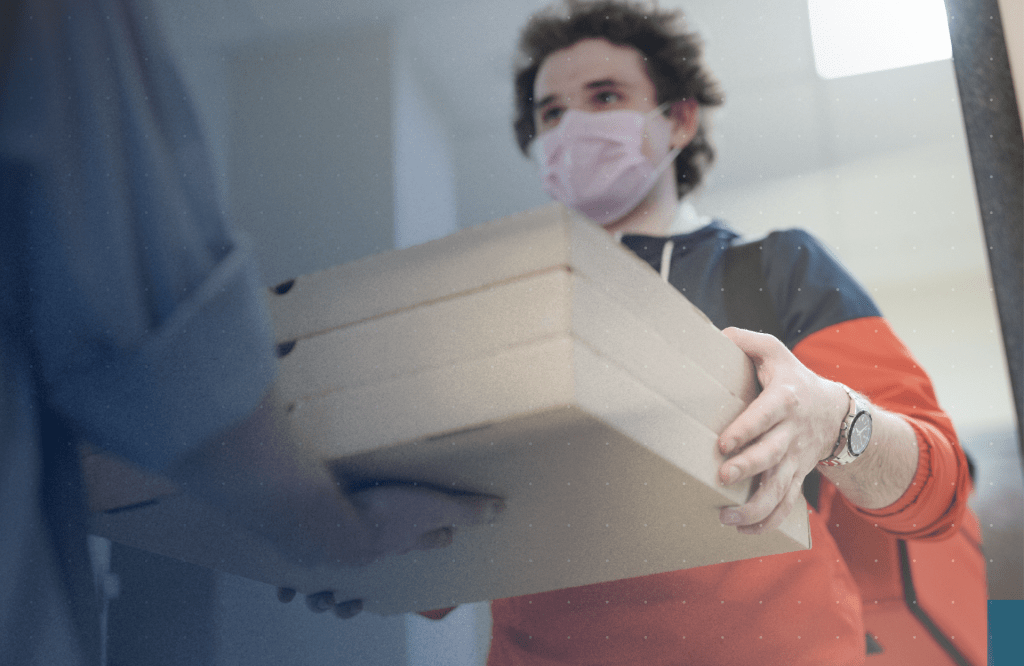 Delivery person wearing a mask and holding three boxes, handing them off to another person